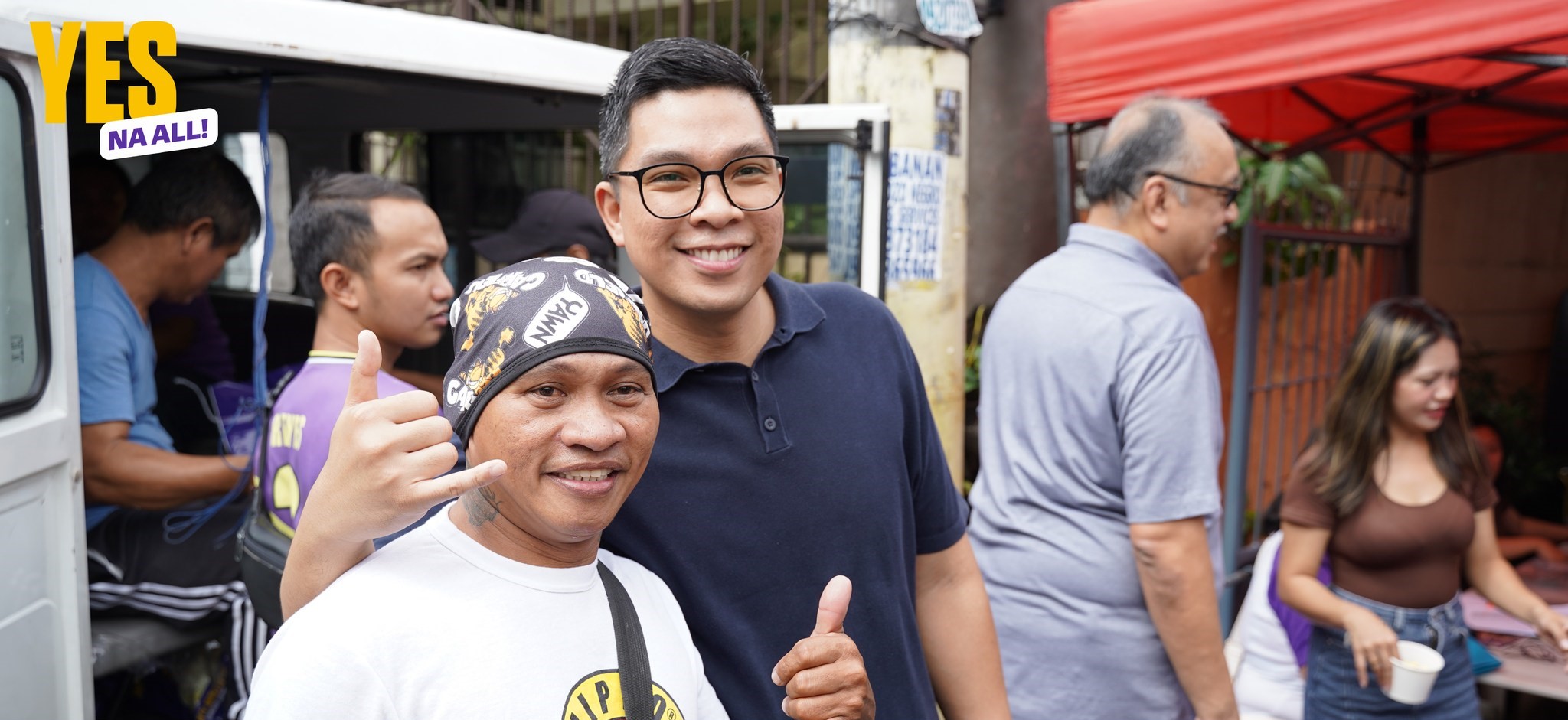 Councilor Anton Reyes poses with a local resident, both flashing a "shaka" gesture during a public community event in Quezon City.