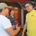 Anton Reyes greeting a resident during a community walk with supporters nearby.