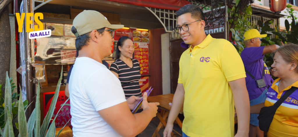 Anton Reyes greeting a resident during a community walk with supporters nearby.