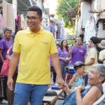 Anton Reyes holding hands with a smiling elderly woman during a community visit in a residential alley.