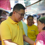 Anton Reyes smiling and speaking with a market vendor during a community visit.